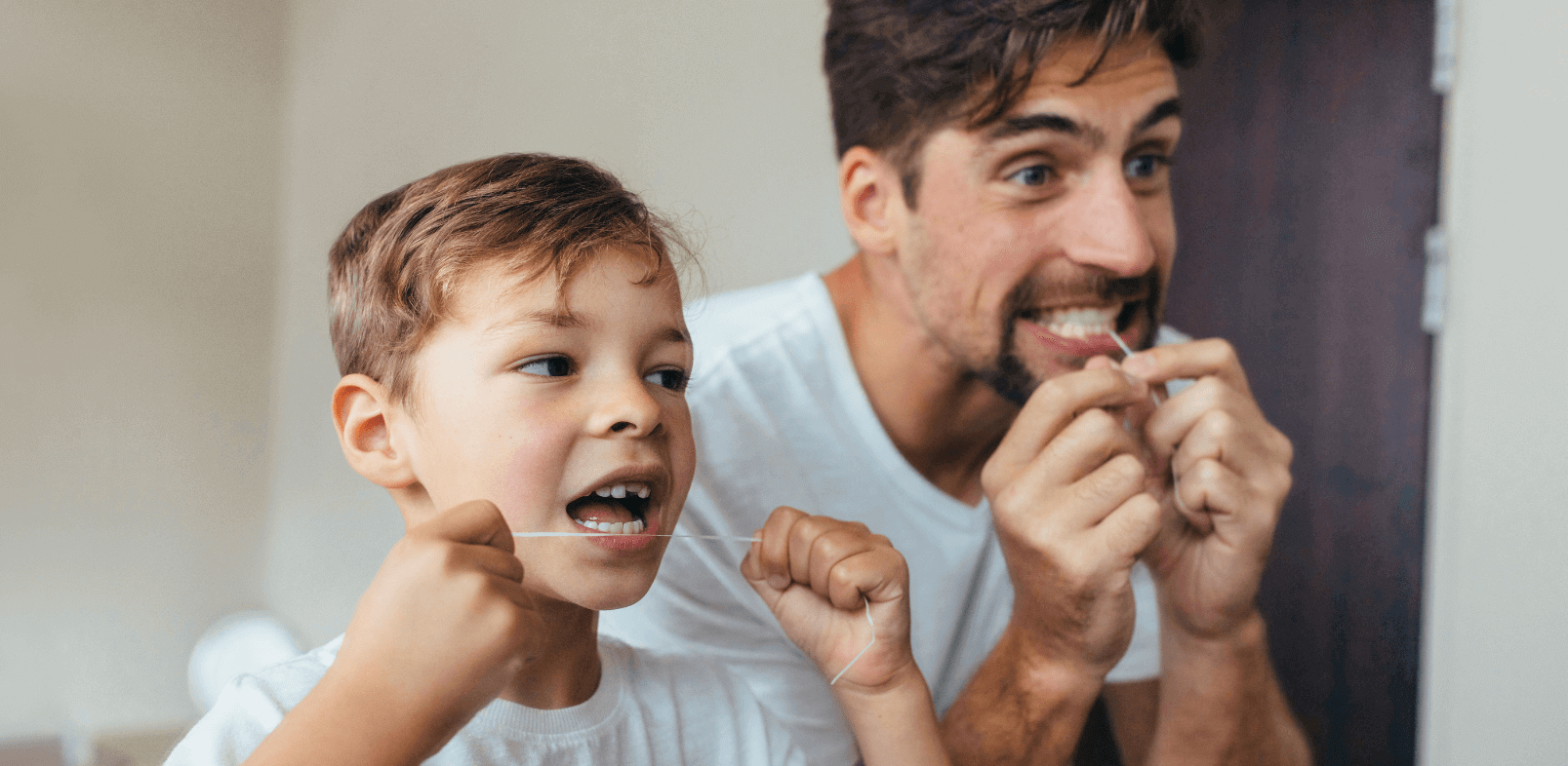 Dad and son flossing their teeth in the mirror