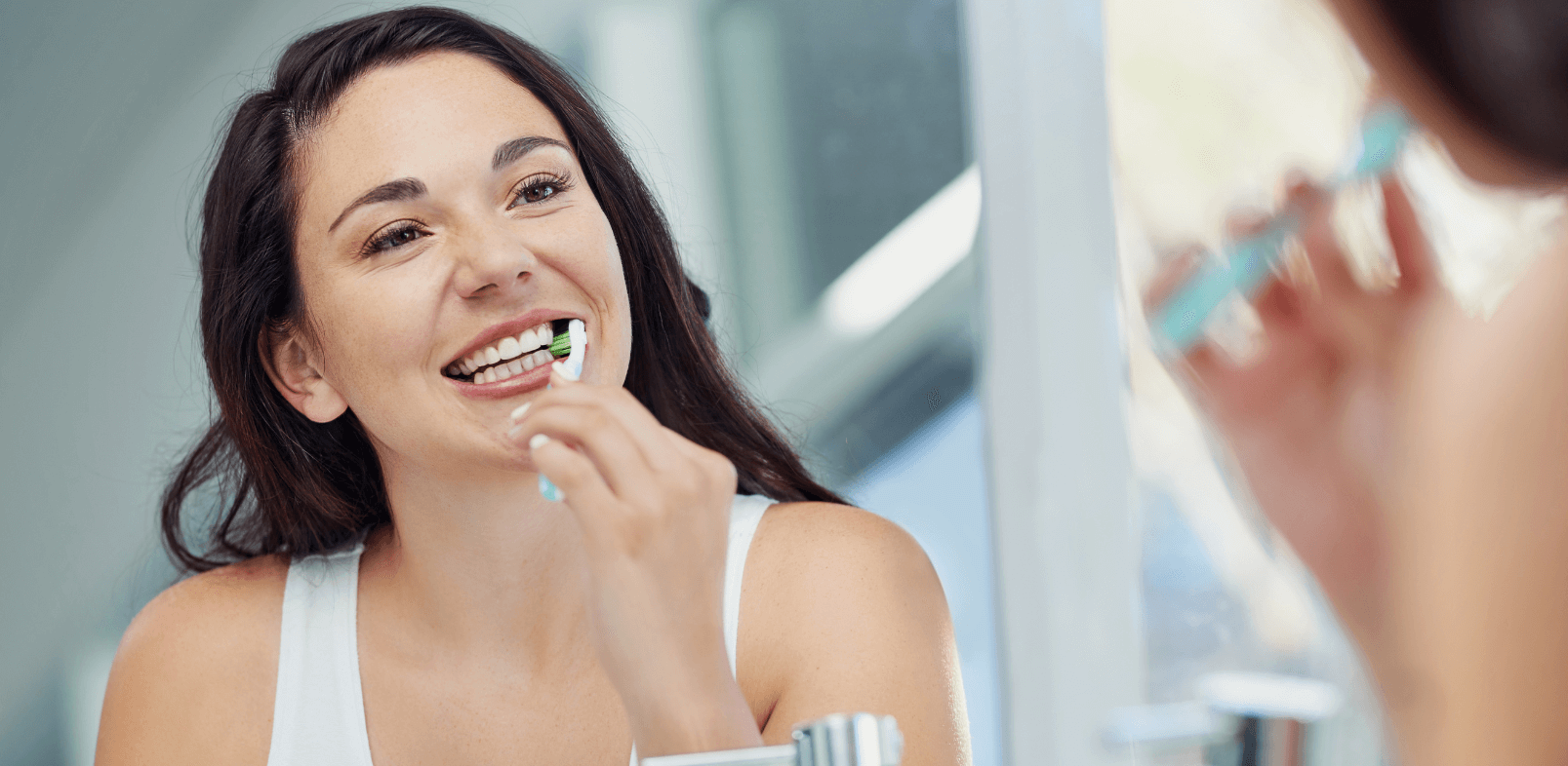 Brunette woman brushing her teeth in the mirror
