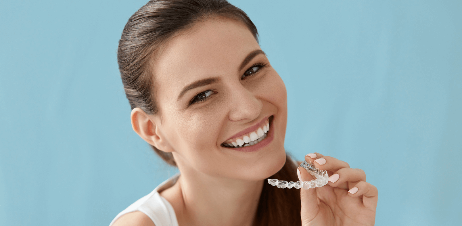 Brunette lady putting Invisalign braces into her mouth whilst smiling