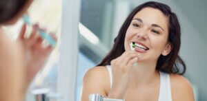 Woman with Invisalign brushing her teeth in the mirror in Ripon