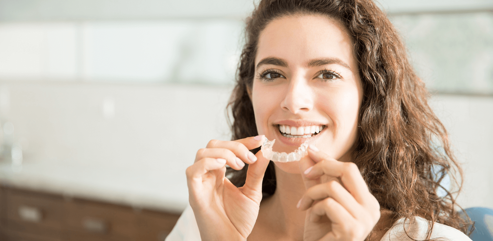 headshot of woman smiling while holding Invisalign clear braces