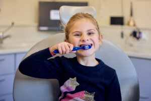 Young girl age six at ease, independently happily brushing her teeth in dental chair at Boroughbridge Dental Centre near Ripon.